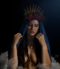 Portrait of young woman standing against black background