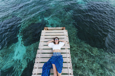 Happy woman with hands behind head lying on jetty during vacation