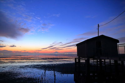 Stilt house on river against sky at sunset