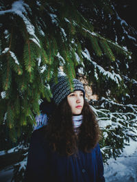 Portrait of a beautiful girl with curly brown hair against a background of fir branches. 