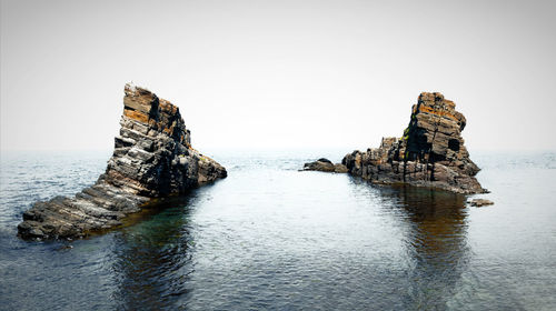 Rock formation in sea against clear sky