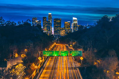 Light trails on illuminated cityscape against sky at night