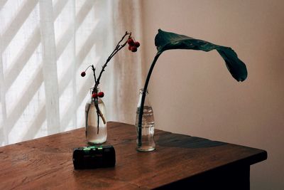 Red rose in vase on table against wall at home