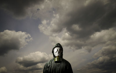 Portrait of person wearing gas mask while standing against cloudy sky
