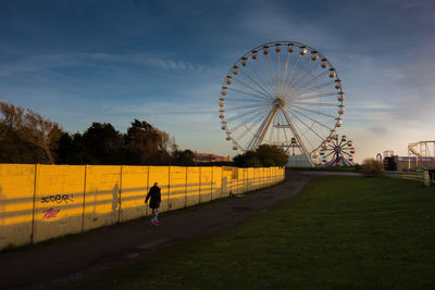 Rear view of woman skating on road by ferris wheel against sky