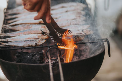 Cropped hand of man preparing fish on barbecue grill