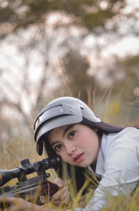 Portrait of young woman aiming gun while lying on grassy field