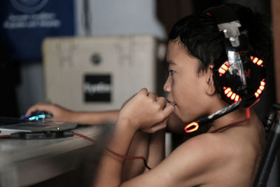 Side view of shirtless boy playing video game over laptop at home