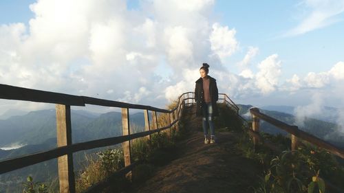 Woman on footbridge against sky