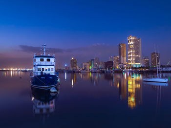 Illuminated buildings by river against sky at dusk