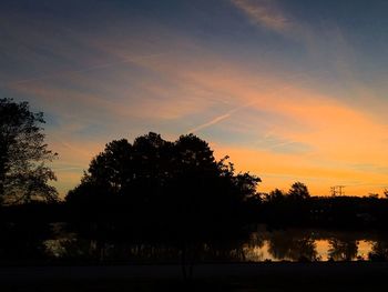 Silhouette trees on landscape against orange sky