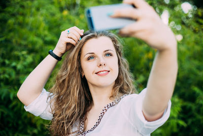 Young woman taking selfie through smart phone against plants