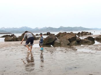 Men walking on rocks by sea against clear sky