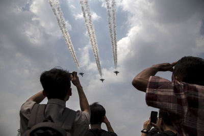 Rear view of people photographing airshow against sky