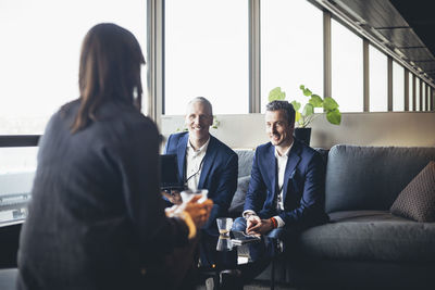 Businessmen with laptop looking at female colleague while sitting on sofa in office