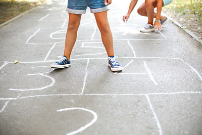 Low section of girls playing hopscotch on road