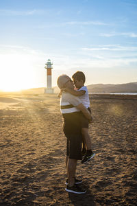 Side view of grandfather and grandson embracing against lighthouse