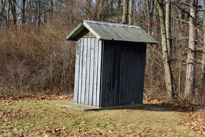 Outhouse by trees on field during sunny day