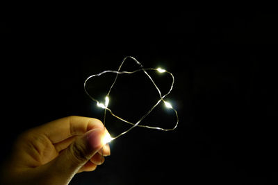 Cropped hand holding illuminated star shape string against black background