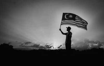 Low angle view of silhouette man with malaysia flag standing against cloudy sky