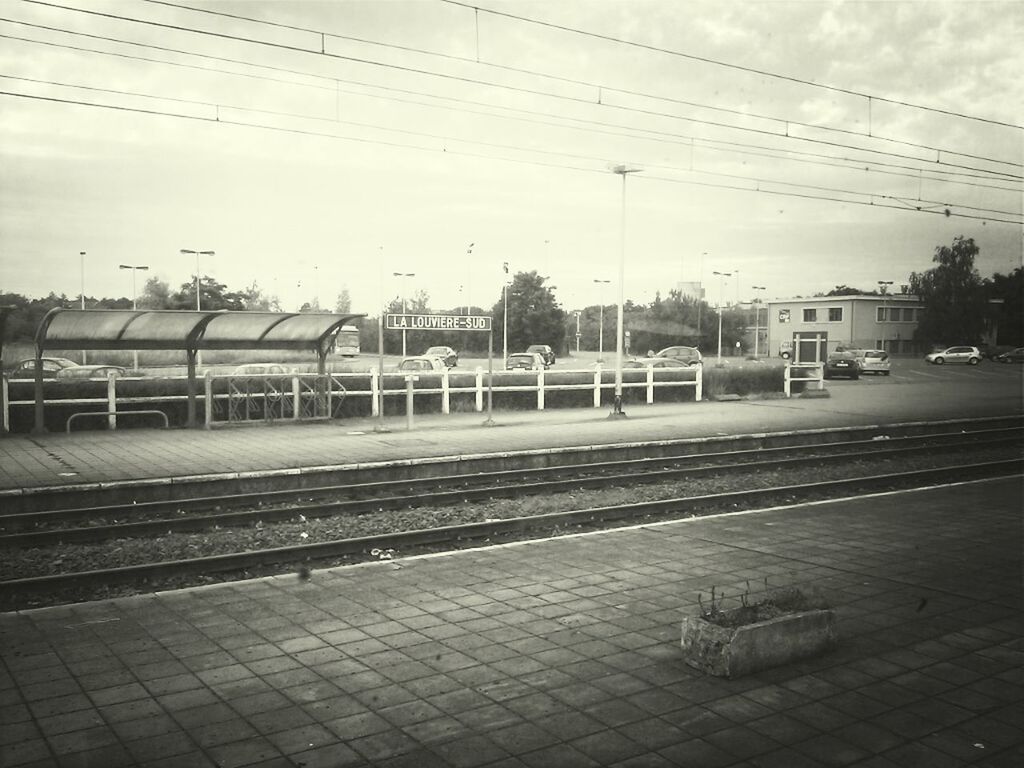 railroad track, transportation, power line, sky, built structure, building exterior, railroad station platform, rail transportation, architecture, street, railroad station, road, electricity pylon, cable, public transportation, city, empty, outdoors, day, no people