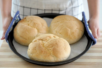 Woman showing three homemade loaves of bread in baking tray freshly baked