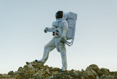 Low angle view of an astronaut standing on rock against clear sky