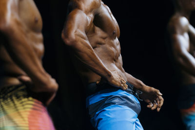 Midsection of shirtless athletes against black background