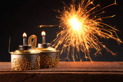 Close-up of oil lamps and sparkler on wooden table against black background