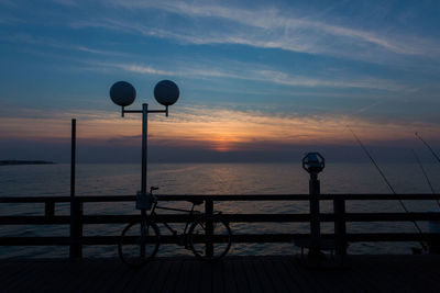 Bicycle parked on pier against sea during sunset