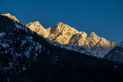 Low angle view of snowcapped mountains against clear blue sky