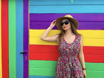 Young woman wearing sunglasses standing against multi colored wall