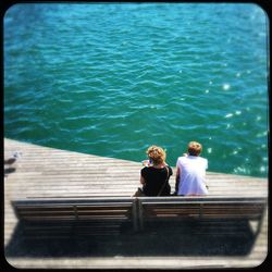 Rear view of women sitting on railing against sea