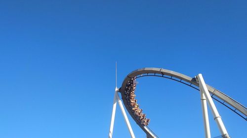 Low angle view of rollercoaster against clear blue sky