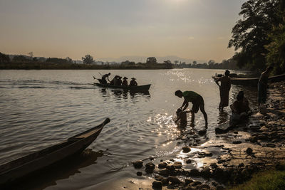 People in lake against sky during sunset