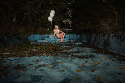 Young woman with balloons sitting at park during night