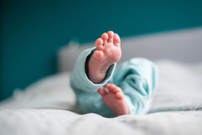 Low section of baby lying on bed at home