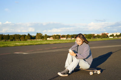 Portrait of young woman sitting on road against sky