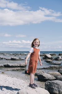 Red-haired girl standing on stone at beach