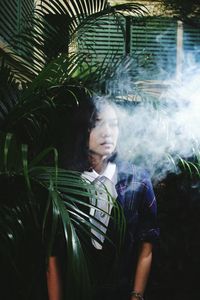 Woman exhaling smoke against trees