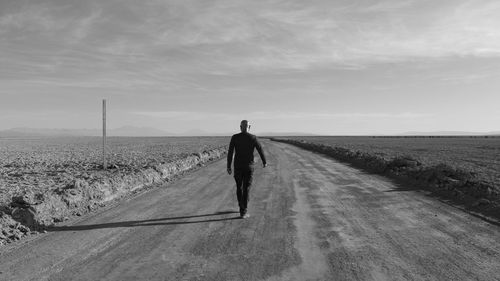 Rear view of man walking on field against sky