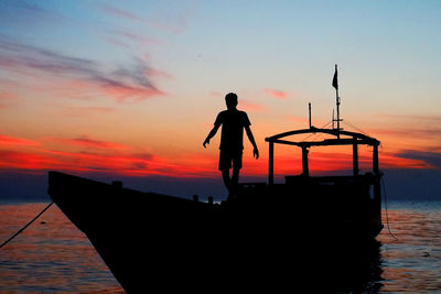 Silhouette man standing on fishing boat in sea against sky during sunset