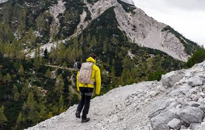 Rear view of hiker wearing hiking clothes and gear, walking on rocky path in mountains