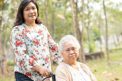 Portrait of smiling woman with handicapped mother on wheelchair against trees