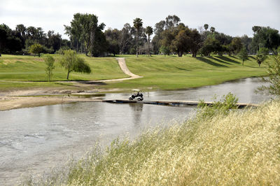 Scenic view of golf course by lake against sky