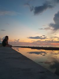 Woman sitting on beach against sky during sunset