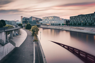 Canal by buildings against cloudy sky during sunset