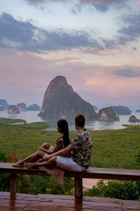 Rear view of woman sitting on bench against scenic sky