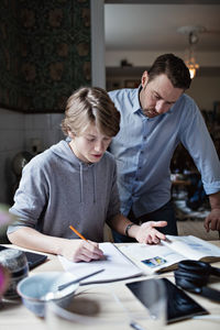 Father looking at son doing homework on table