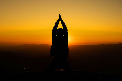 Silhouette man standing by house against sky during sunset